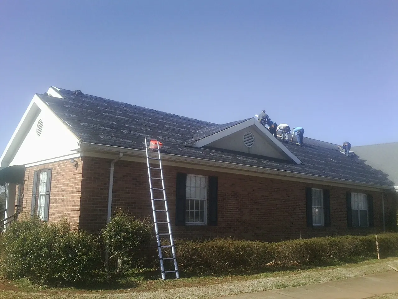 Crew tearing shingles off a brick ranch roof with a ladder set — Metal Roof Repair work by our crew in Berwick