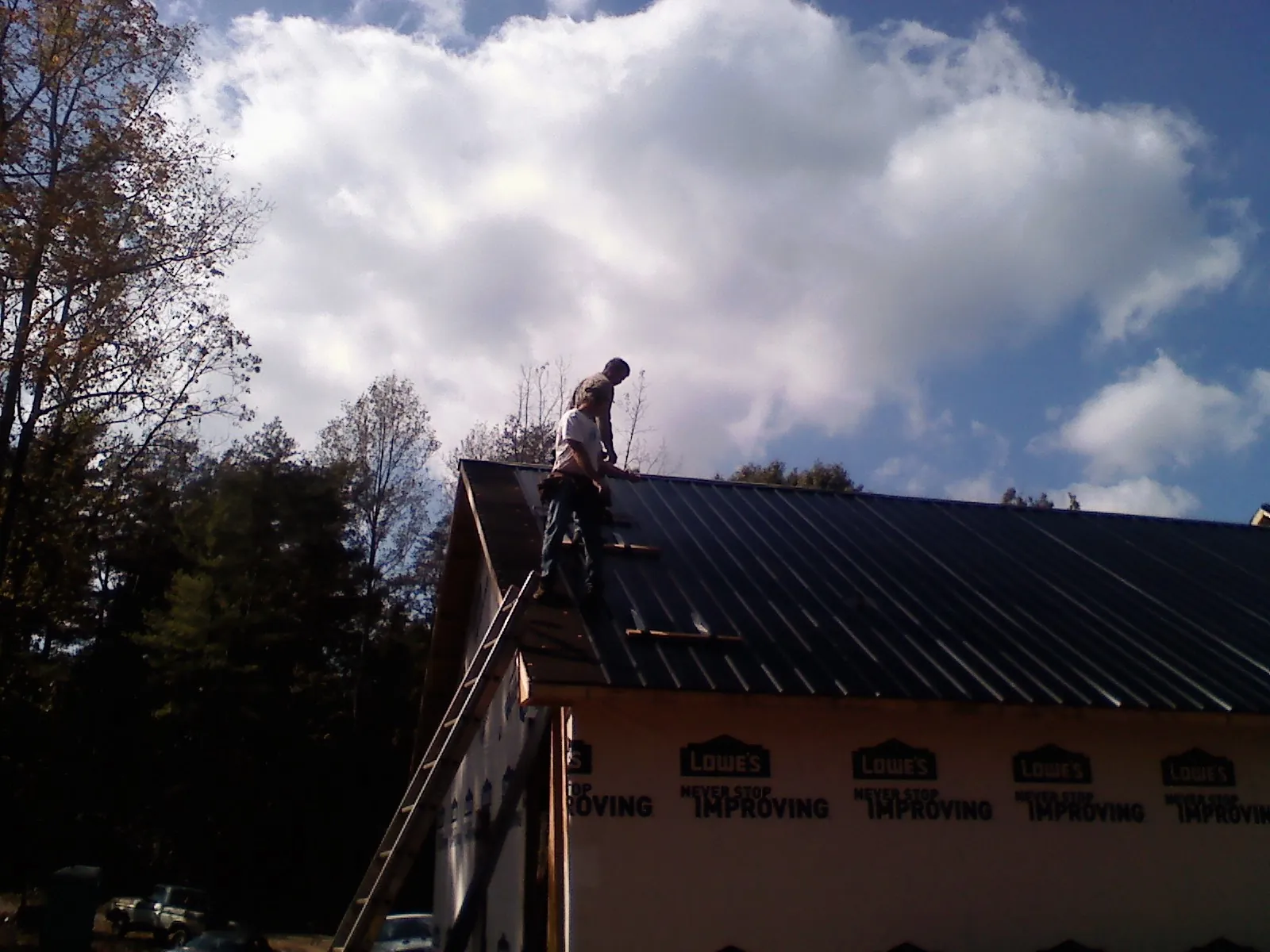 Roofer fastening dark metal panels high against a cloudy sky, from a Roof Inspection job in Berwick